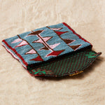 Colorful beaded clutch with brown kanga fabric lining on a sand background