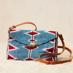 Beaded handbag with geometric pattern and brown leather strap on a beige background