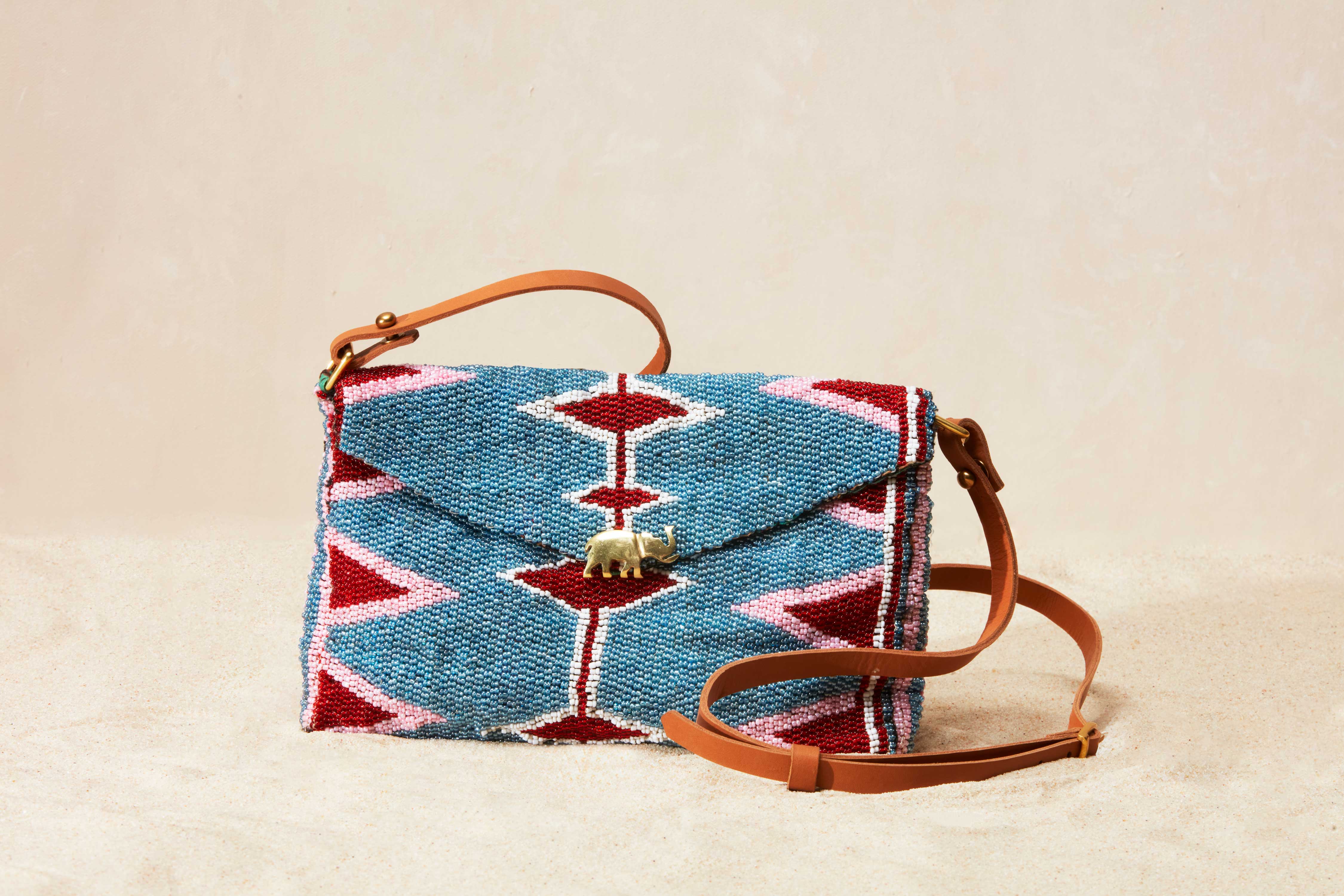 Beaded handbag with geometric pattern and brown leather strap on a beige background