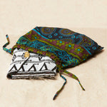 Black and white beaded clutch with brass elephant emblem in a colorful kanga fabric dust bag on a sandy surface