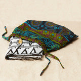 Black and white beaded clutch with brass elephant emblem in a colorful kanga fabric dust bag on a sandy surface