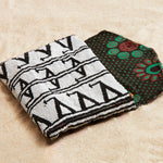 Black and white beaded clutch with colorful kanga fabric lining on a sand background