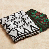 Black and white beaded clutch with colorful kanga fabric lining on a sand background