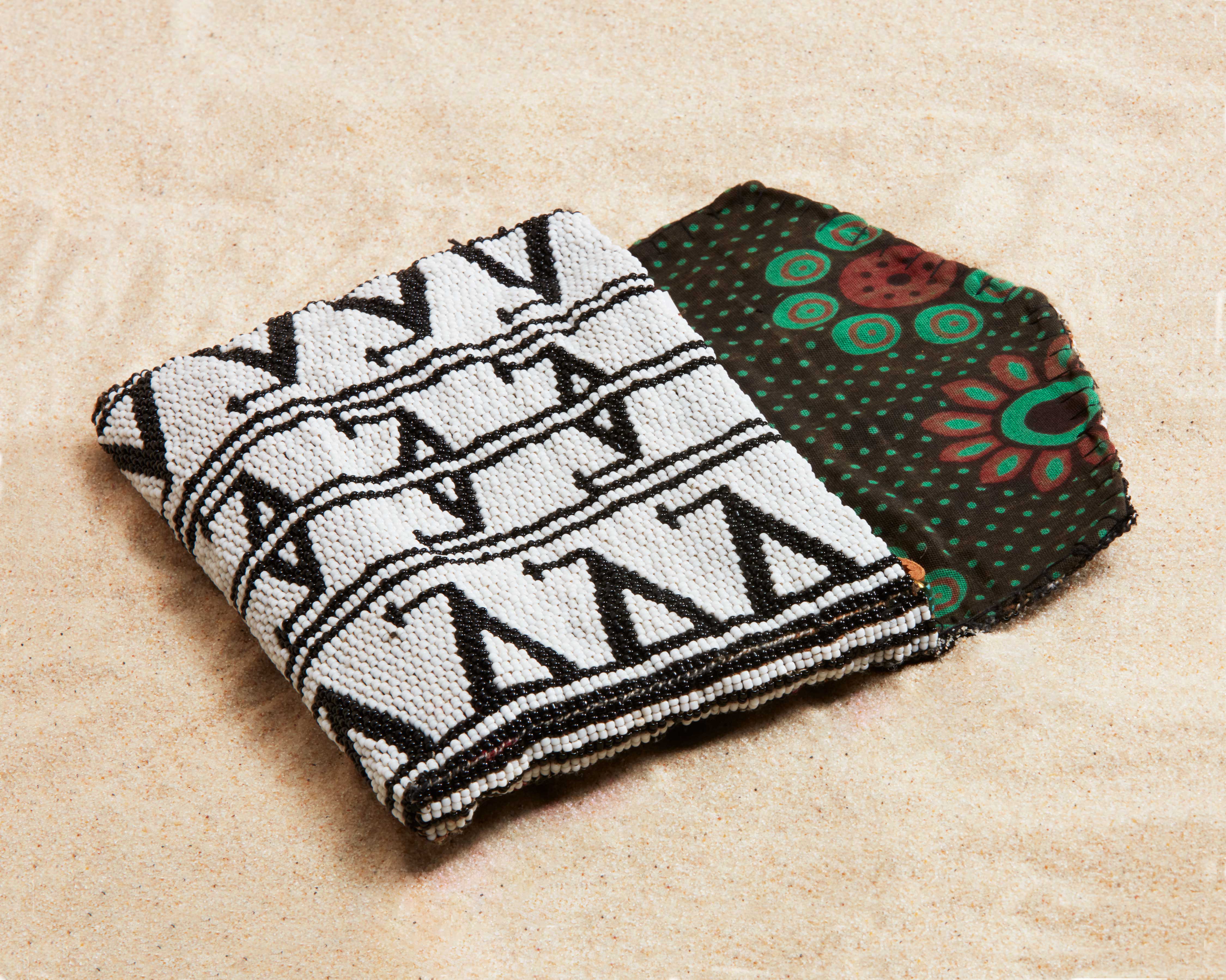 Black and white beaded clutch with colorful kanga fabric lining on a sand background
