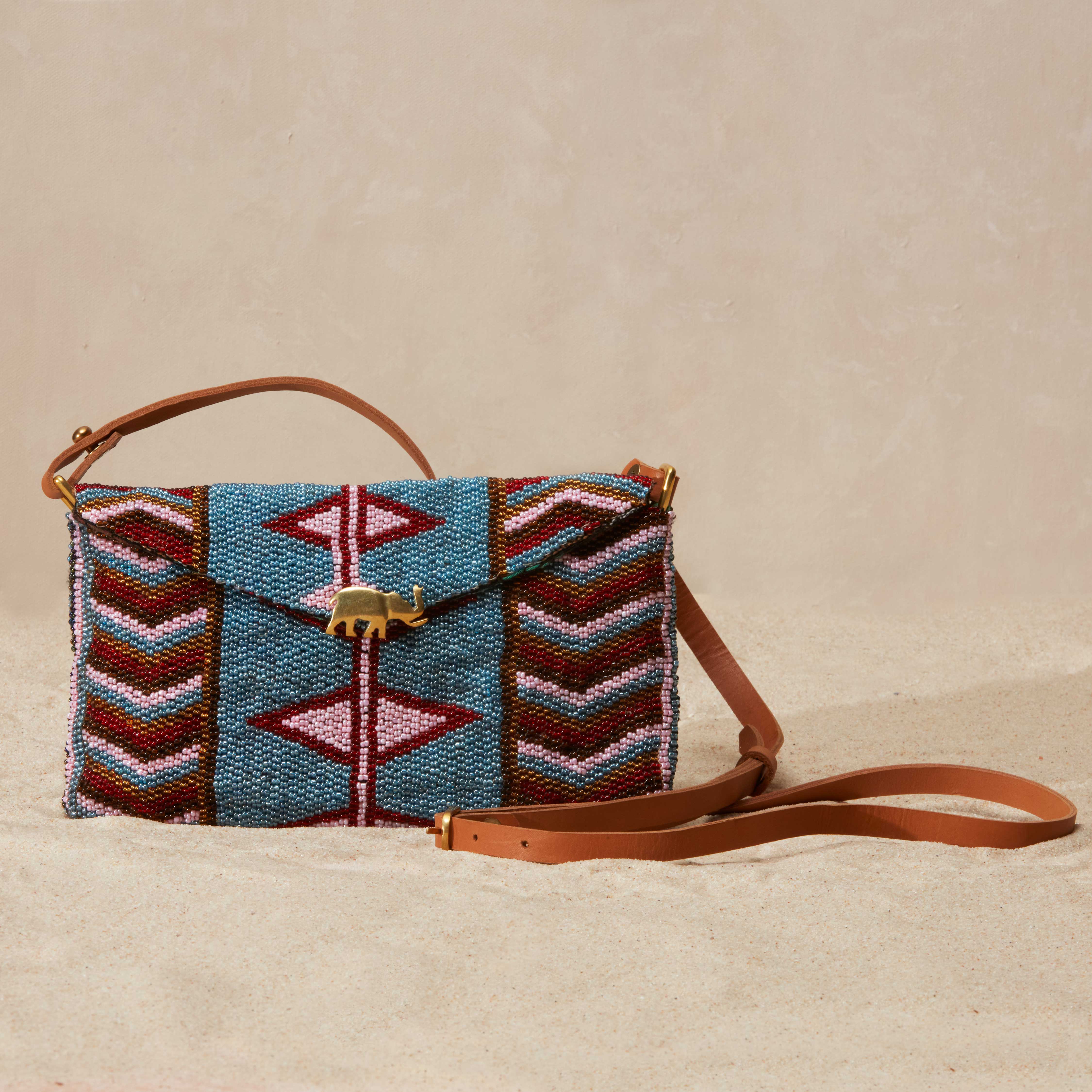 Handbeaded bag with geometric pattern, a brass elephant and brown leather strap on beige background