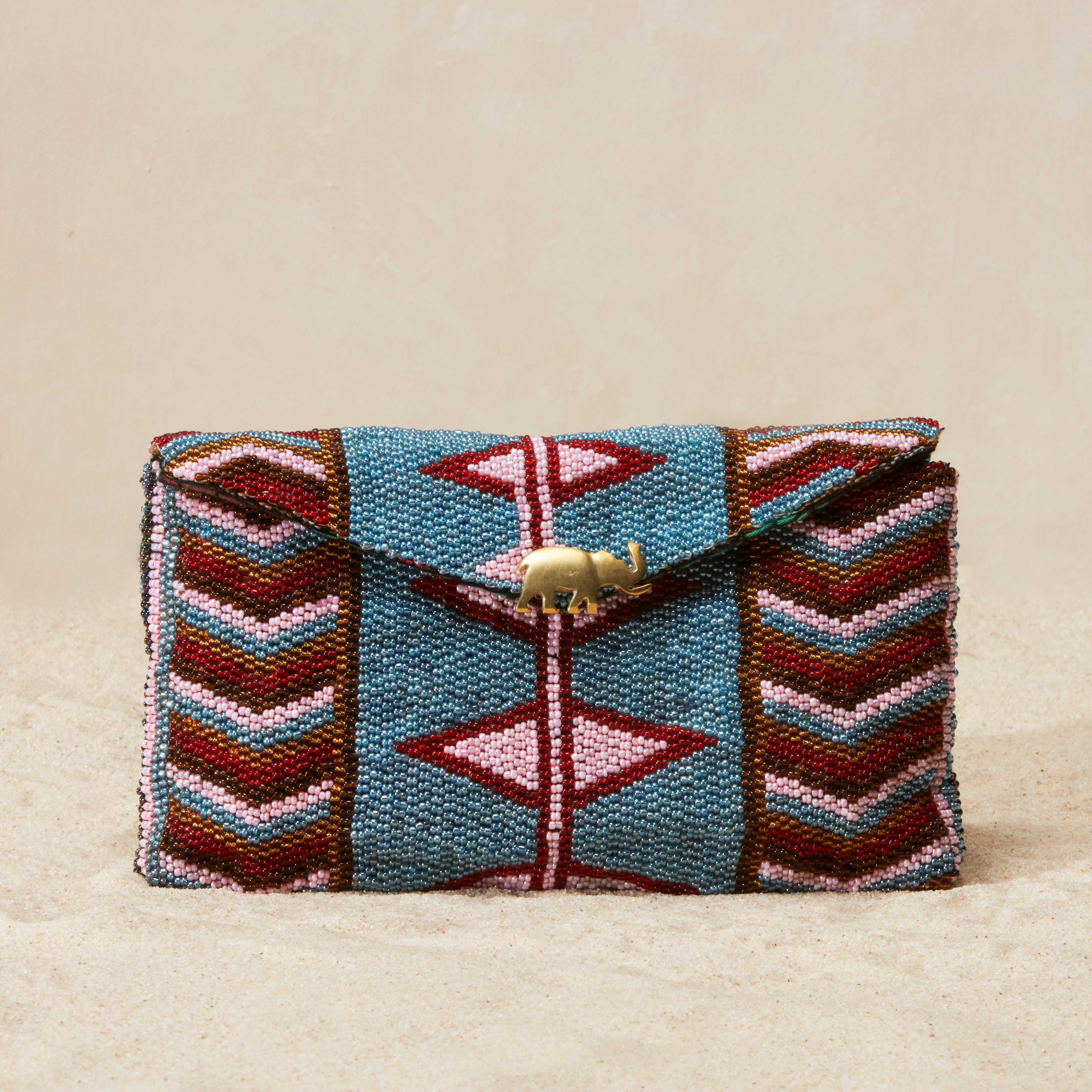 Colorful beaded clutch bag with geometric patterns and a brass elephant on a beige background