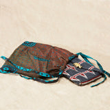 Geometric patterned beaded bag inside a colorful kanga fabric dust bag on a sandy surface
