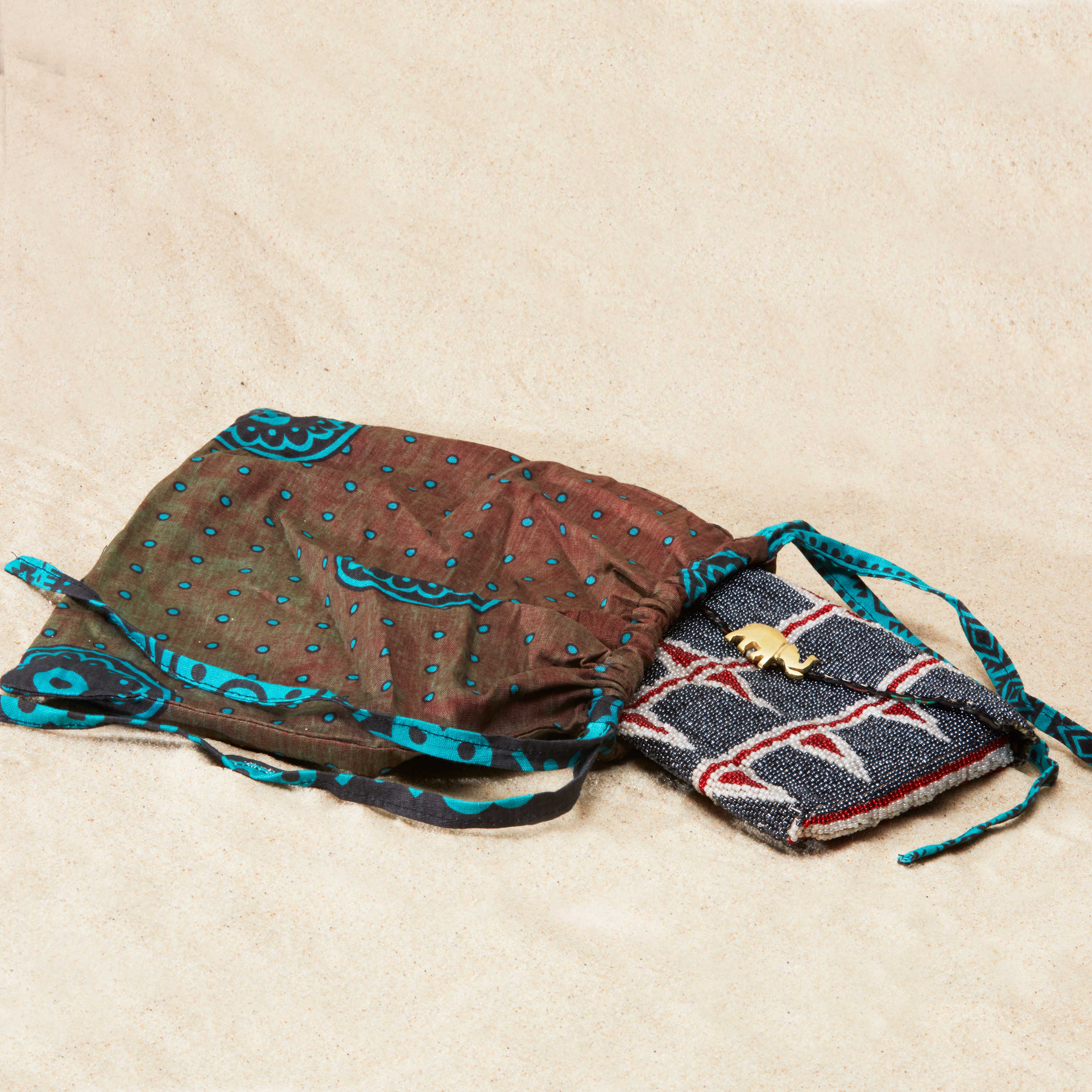 Geometric patterned beaded bag inside a colorful kanga fabric dust bag on a sandy surface