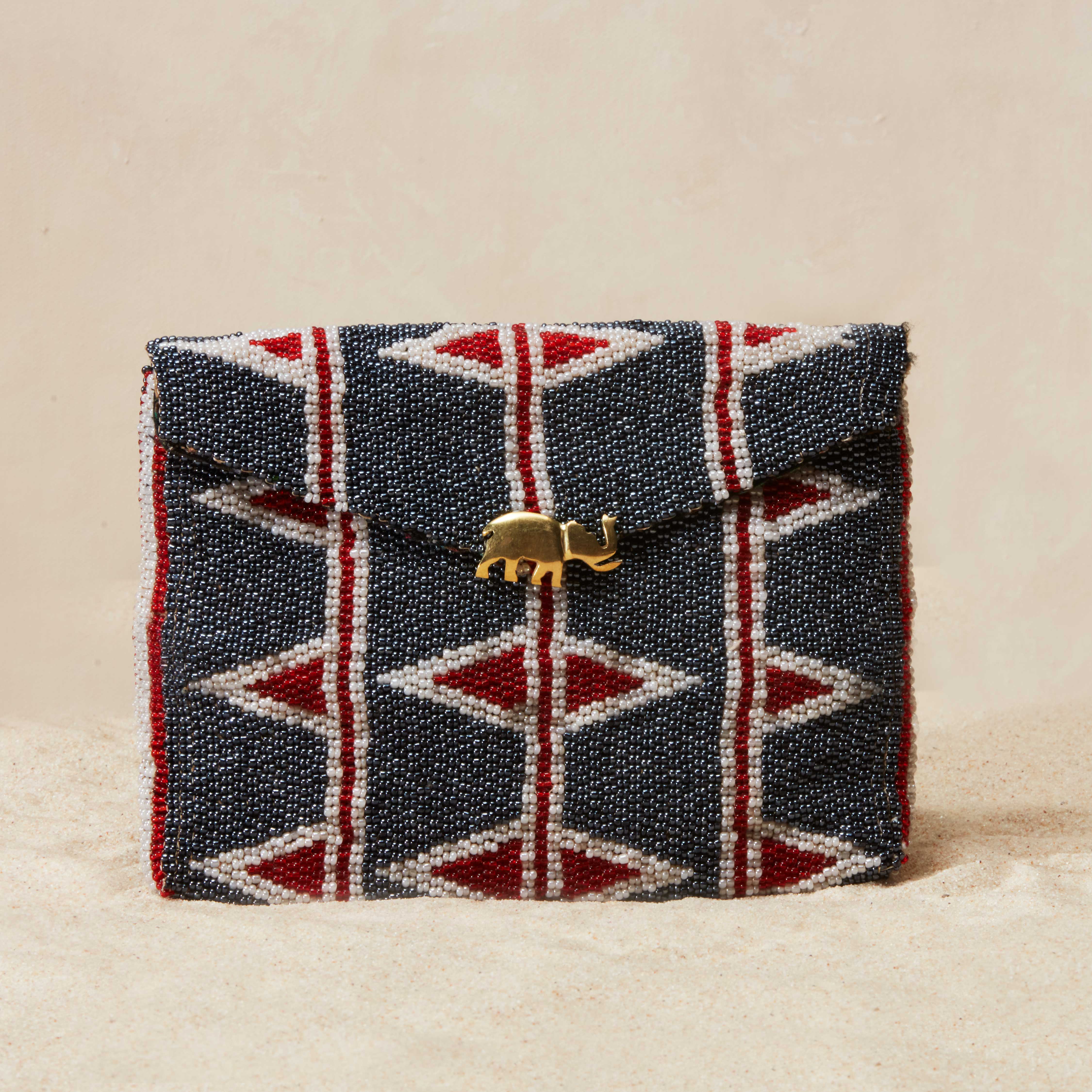 Beaded clutch with geometric pattern and brass elephant on a beige background
