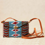 Beaded handbag with colorful pattern and brown leather strap on a beige background