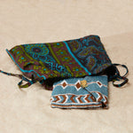 Brown, white and blue beaded clutch in a colorful kanga fabric dust bag on a sandy surface