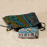 Brown, white and blue beaded clutch in a colorful kanga fabric dust bag on a sandy surface