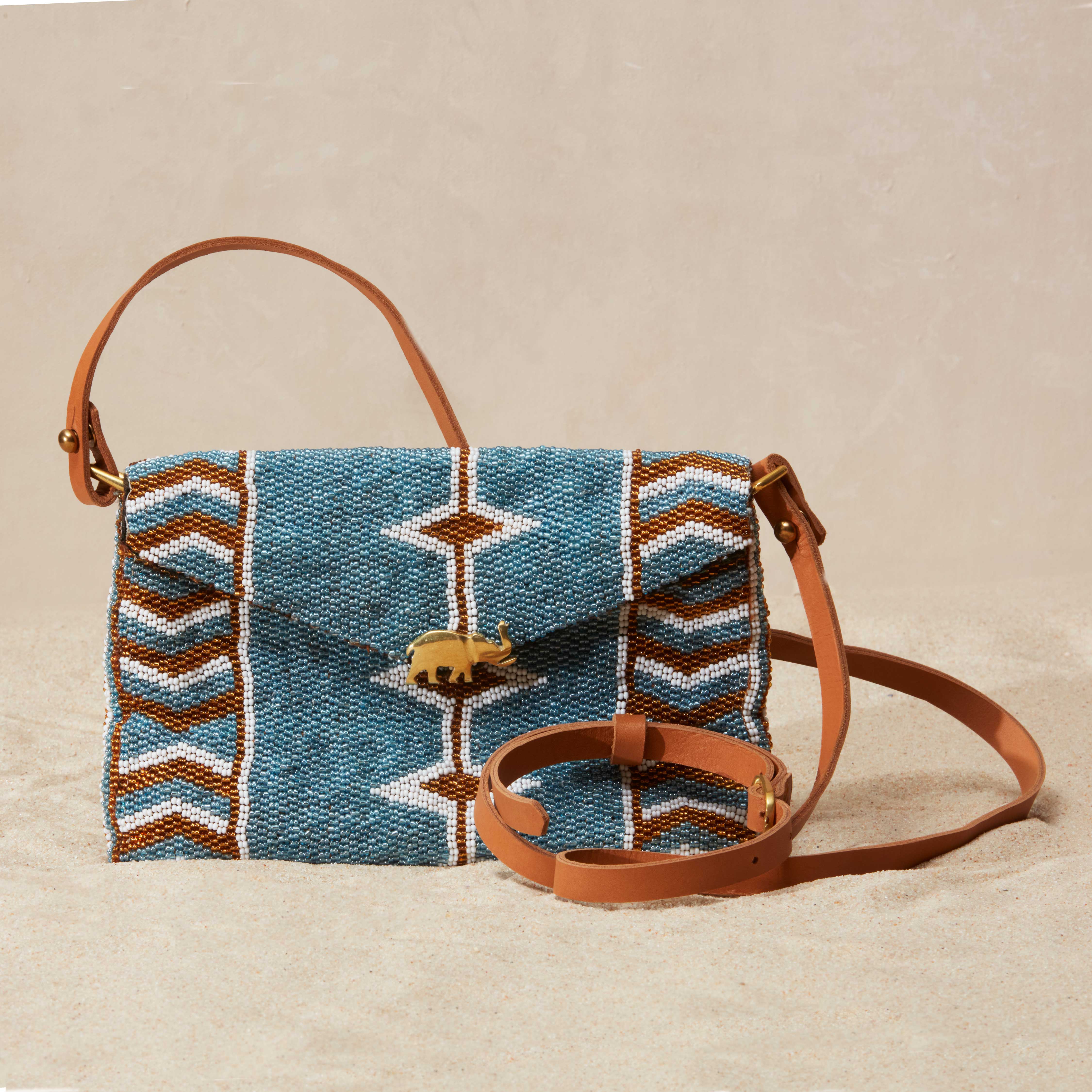 Beaded handbag with blue patterned body and brown leather strap on beige background