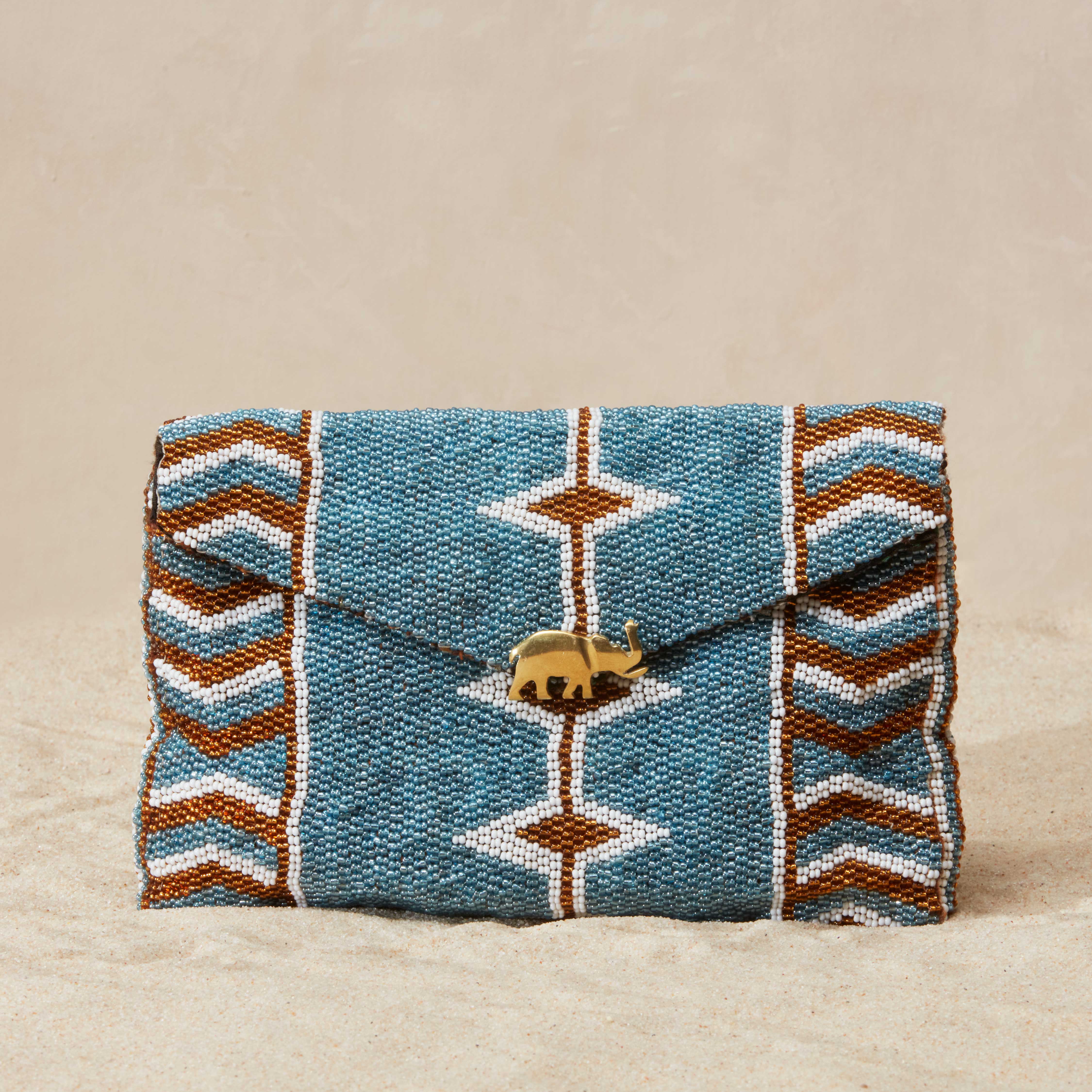Beaded clutch with geometric pattern and brass elephant charm on a sandy beige background