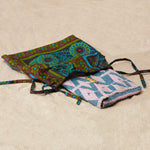 Pink and blue beaded geometric clutch in a colorful kanga dust bag on a sandy surface