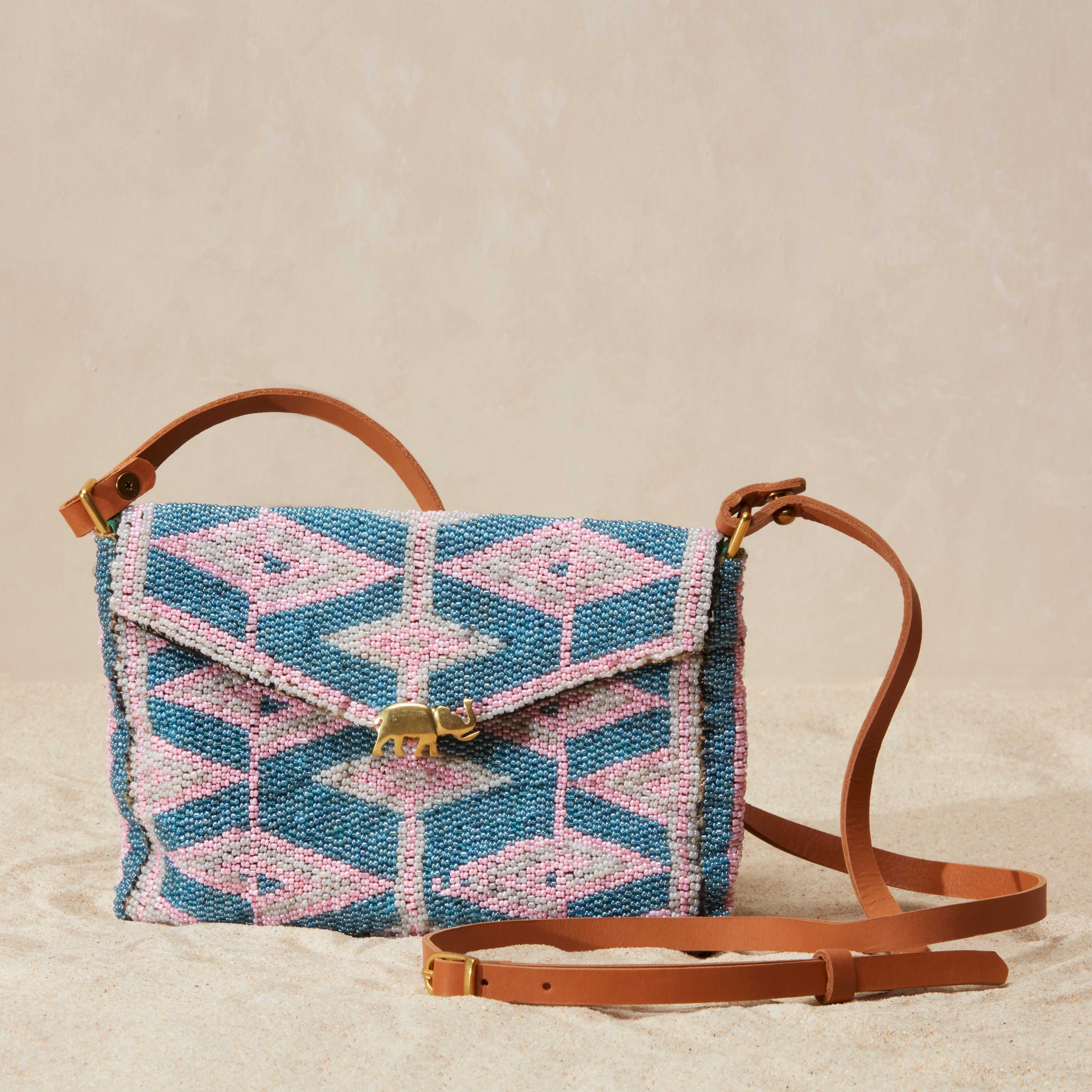 Beaded handbag with geometric pattern and a brass elephant and brown leather strap on a sandy background