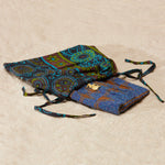 Brown and purple beaded clutch with brass elephant in a pattern kanga fabric dust bag on a sandy surface