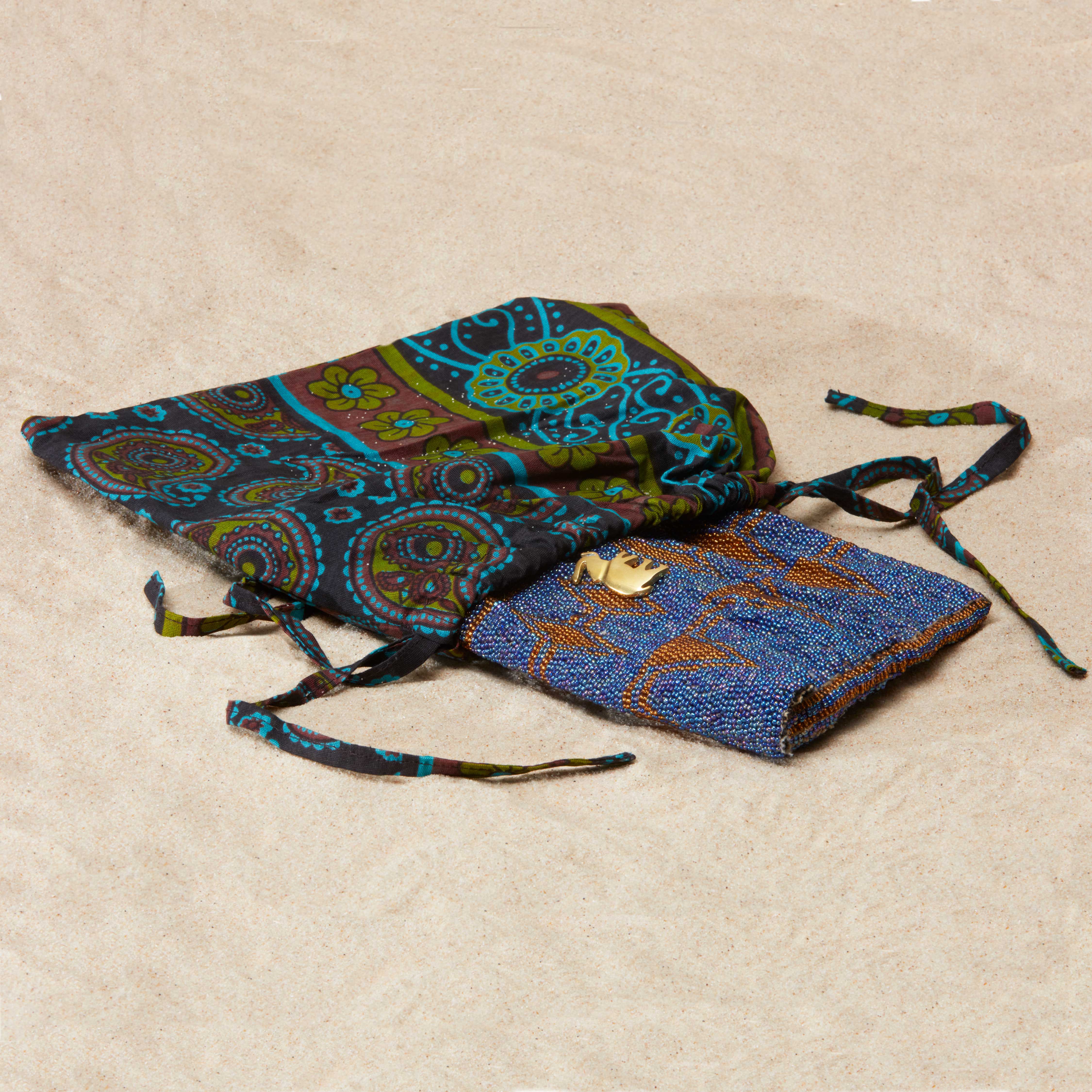 Brown and purple beaded clutch with brass elephant in a pattern kanga fabric dust bag on a sandy surface
