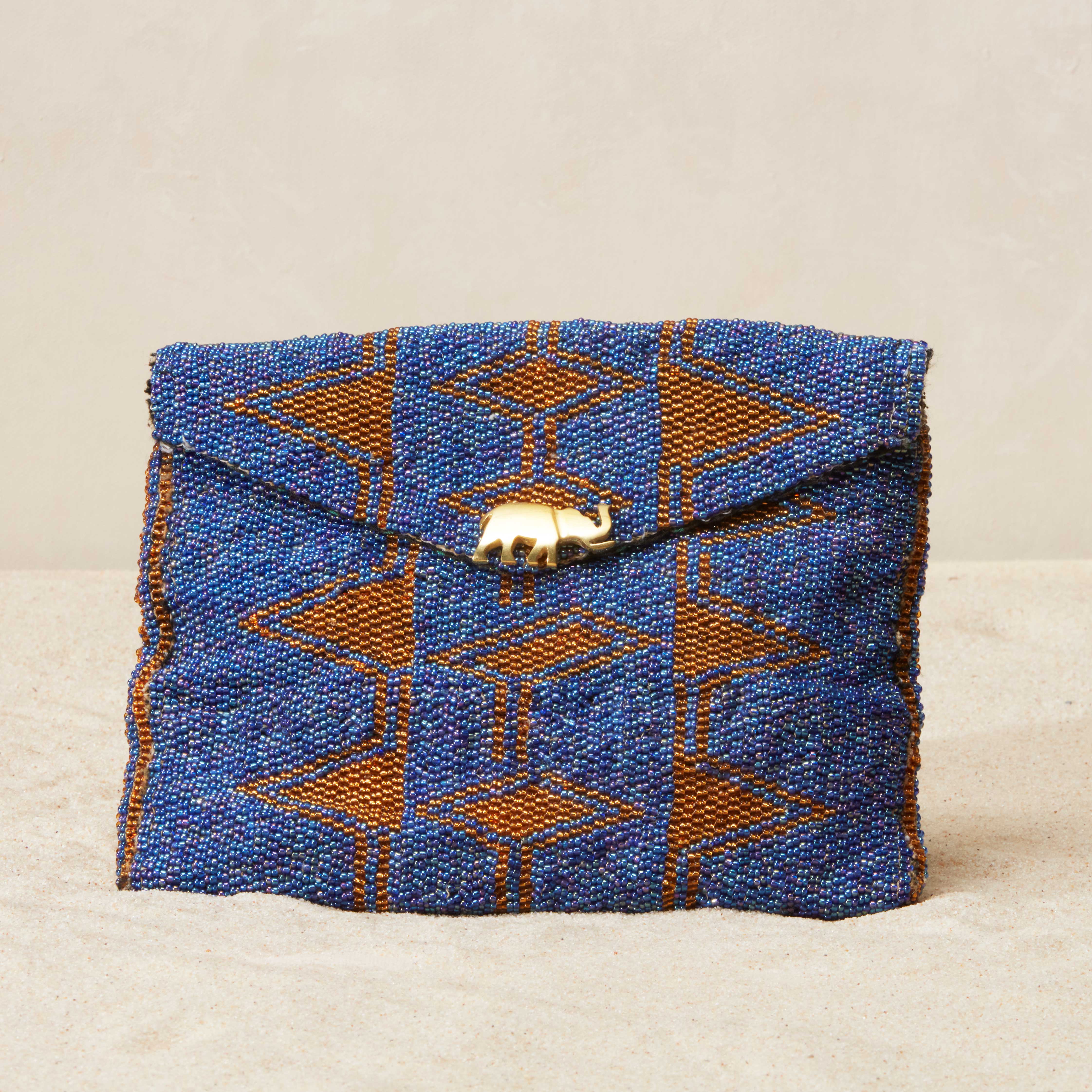 Blue and brown patterned beaded clutch bag with a brass elephant on a beige sand background