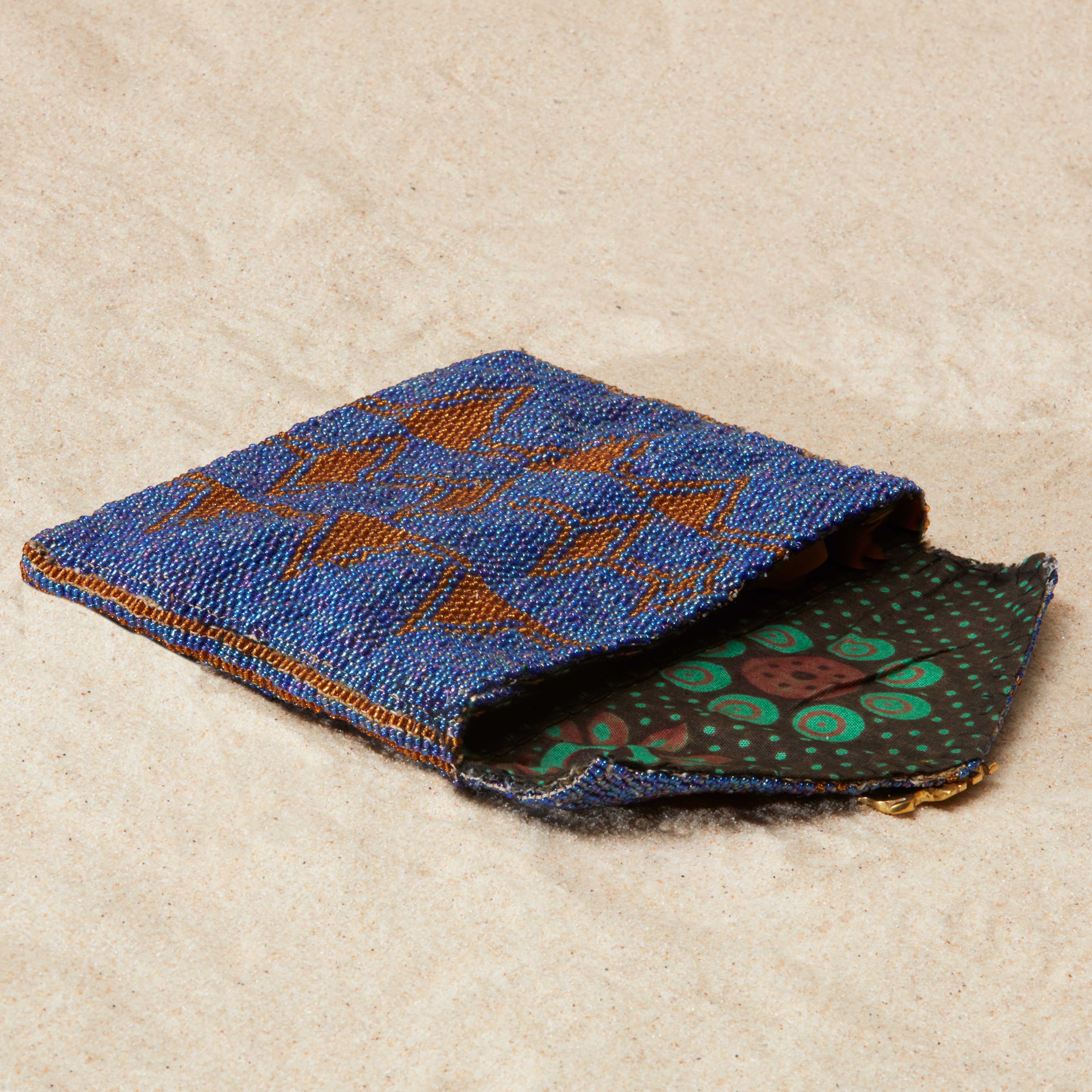 Beaded blue and brown patterned pouch with a green and brown kanga fabric lining on a beige surface