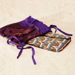 Colorful geometric patterned beaded clutch in a maroon and purple kanga fabric dust bag on a sandy surface