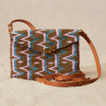 Beaded handbag with a geometric pattern and a brown leather strap on a beige background