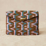 Beaded clutch with geometric pattern  and a brass elephant on a beige background