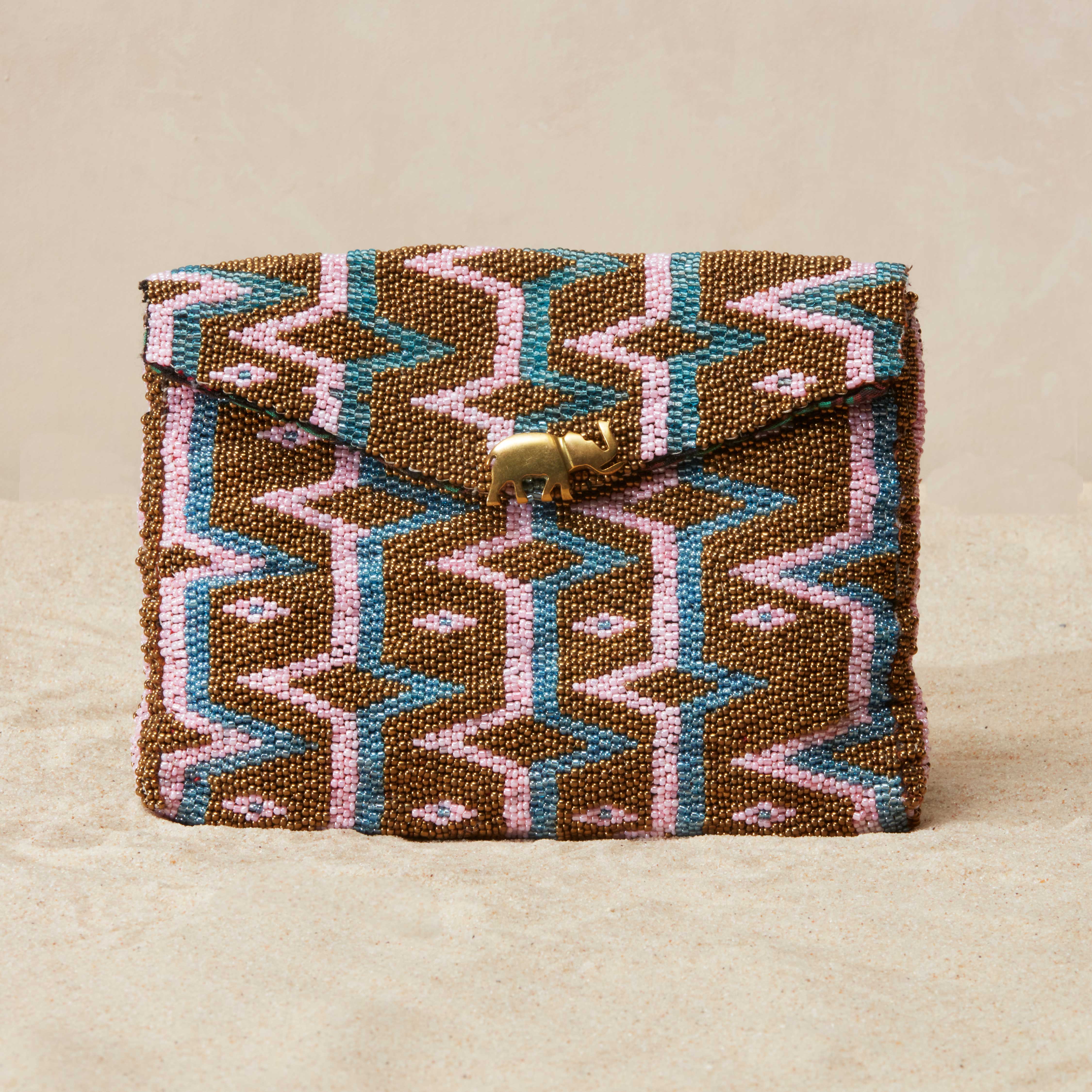 Beaded clutch with geometric pattern  and a brass elephant on a beige background