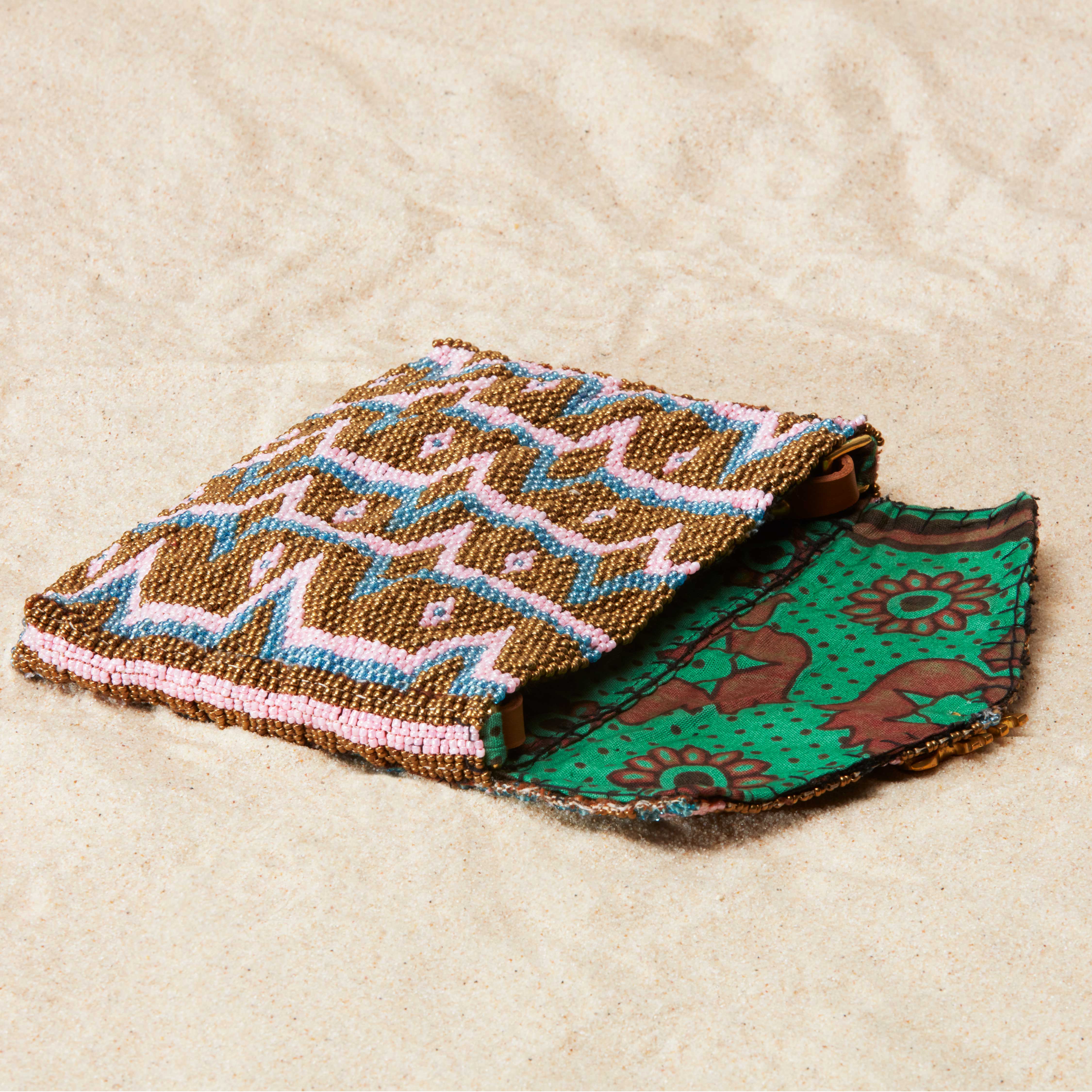 Beaded geometric clutch open showing the colorful green kanga fabric lining on a sand background