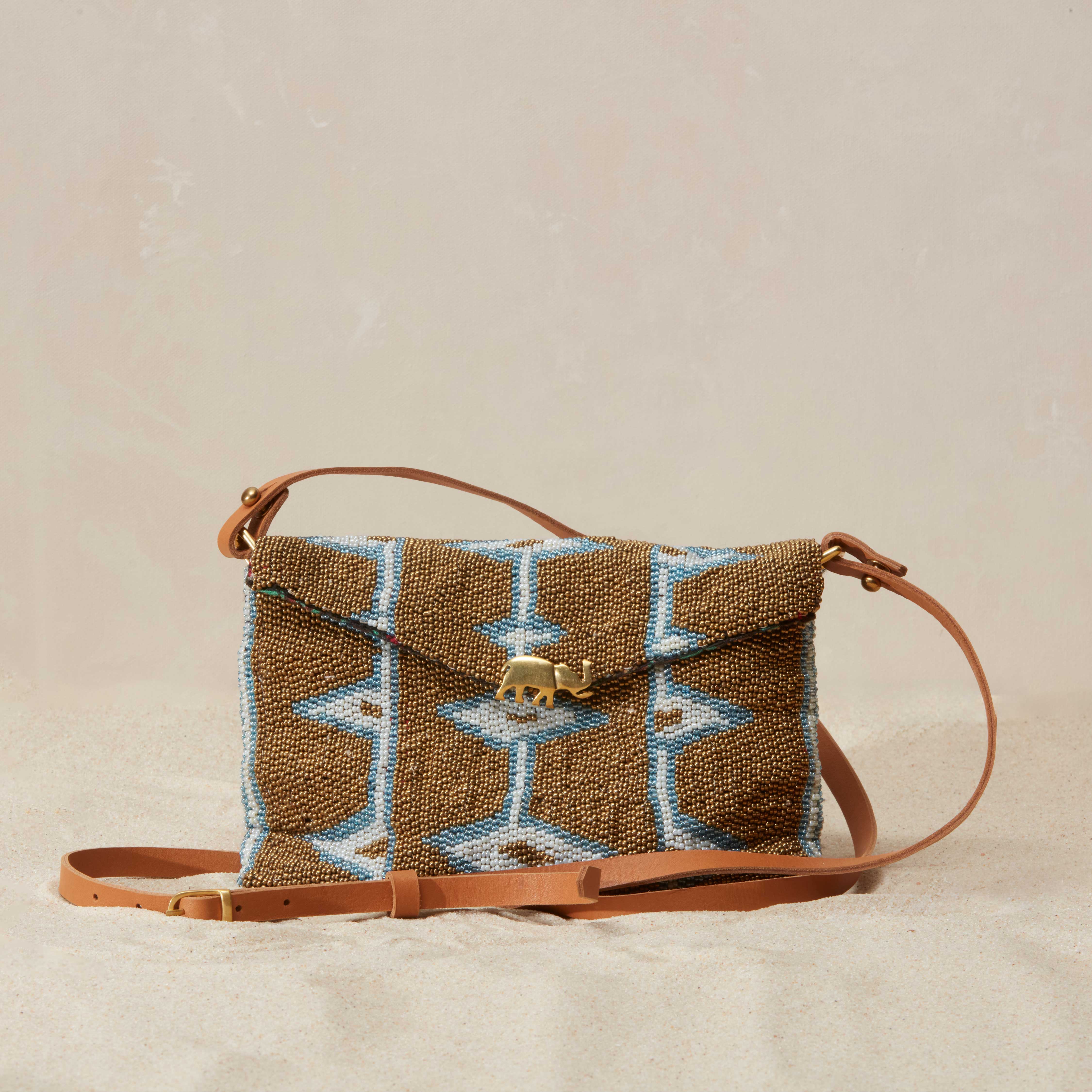Beaded handbag with geometric pattern and leather strap on a beige background