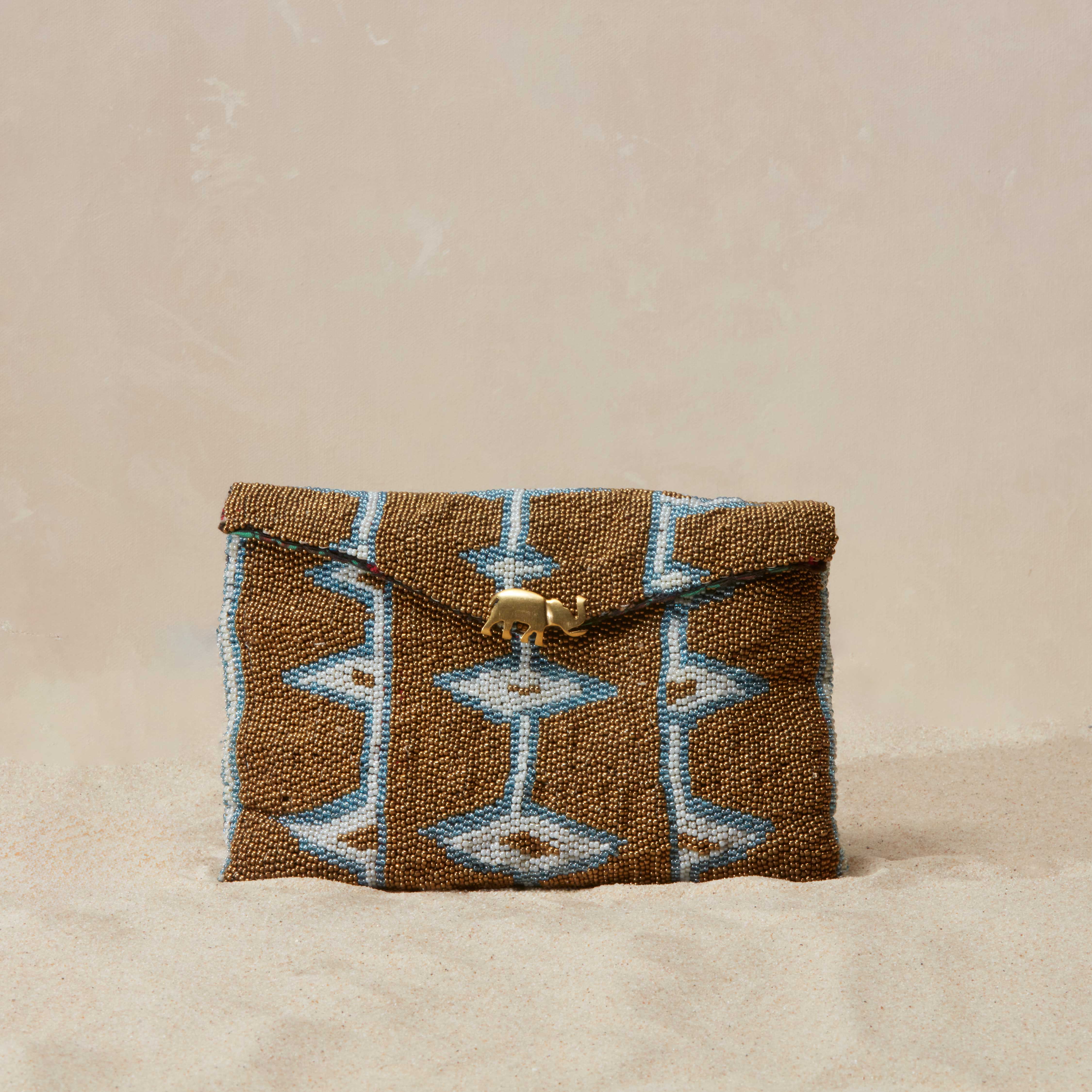 Gold, white and blue beaded pouch with geometric pattern  and brass elephant on a beige background