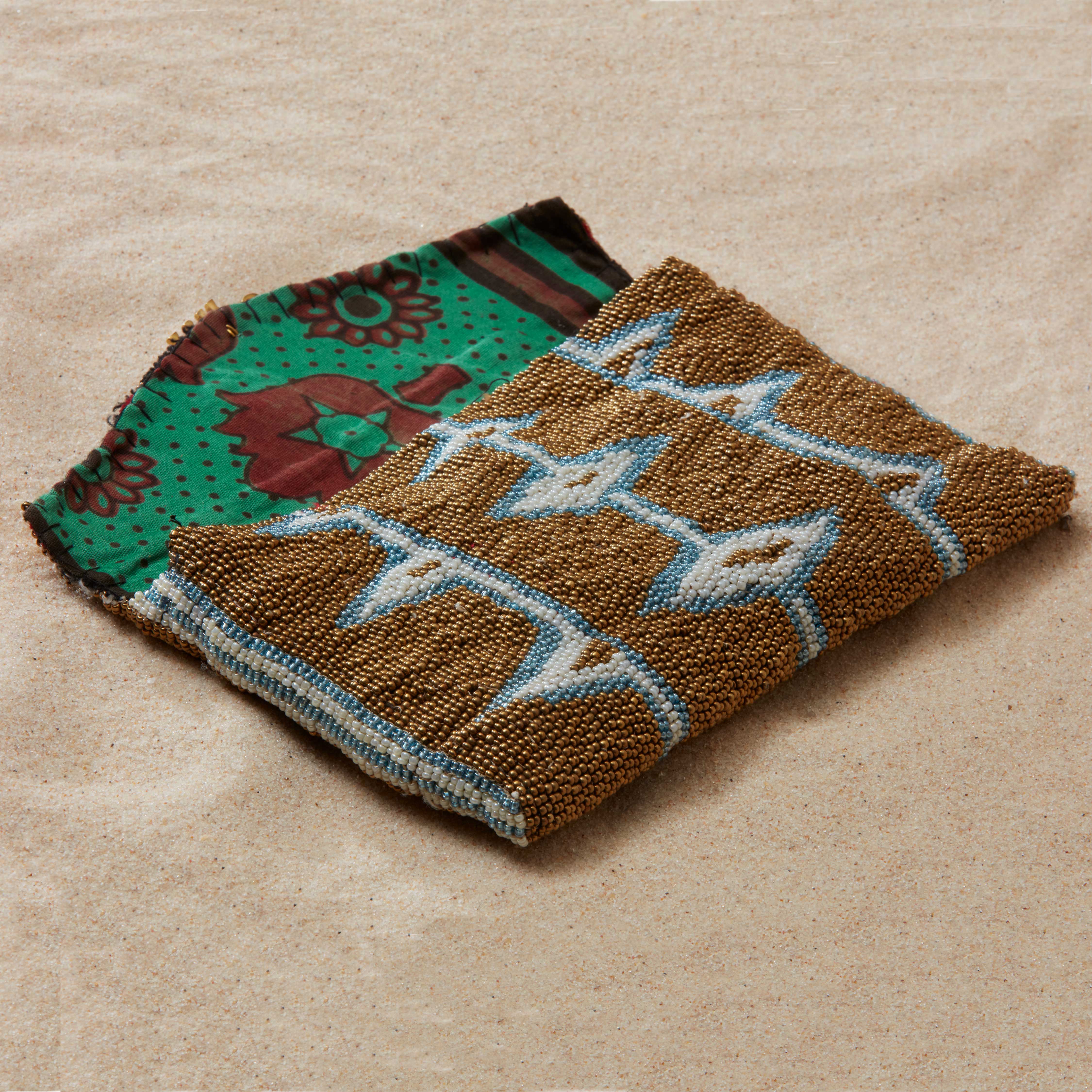 Open beaded clutch with green colorful kanga fabric lining on a sand background