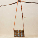 Small beaded geometric handbag with a brown leather strap, hanging on a branch.
