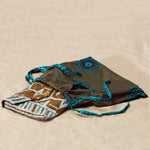 Gold, blue and white beaded geometric patterned clutch in a brown and turquoise colorful kanga dust bag on a sandy surface