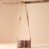 Back view of a small beaded handbag with a geometric pattern and leather strap hanging on a branch