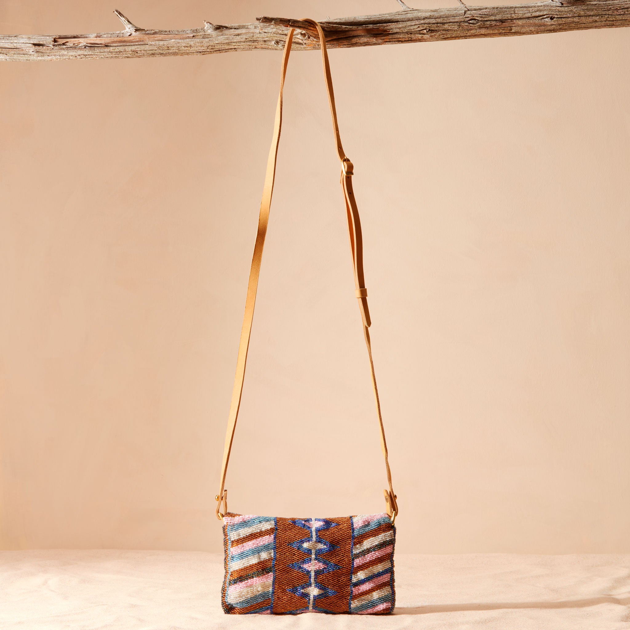 Back view of a small beaded handbag with a geometric pattern and leather strap hanging on a branch