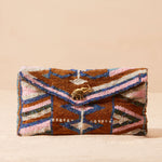 Beaded clutch bag with geometric pattern and brass elephant charm on a beige background