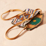 Colorful beaded clutch with brown leather strap, open showing the colorful kanga fabric lining of the bag on a sand background