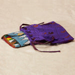 Colorful beaded clutch in a bright purple kanga fabric dust bag on a sand background