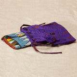 Colorful beaded clutch in a bright purple kanga fabric dust bag on a sand background