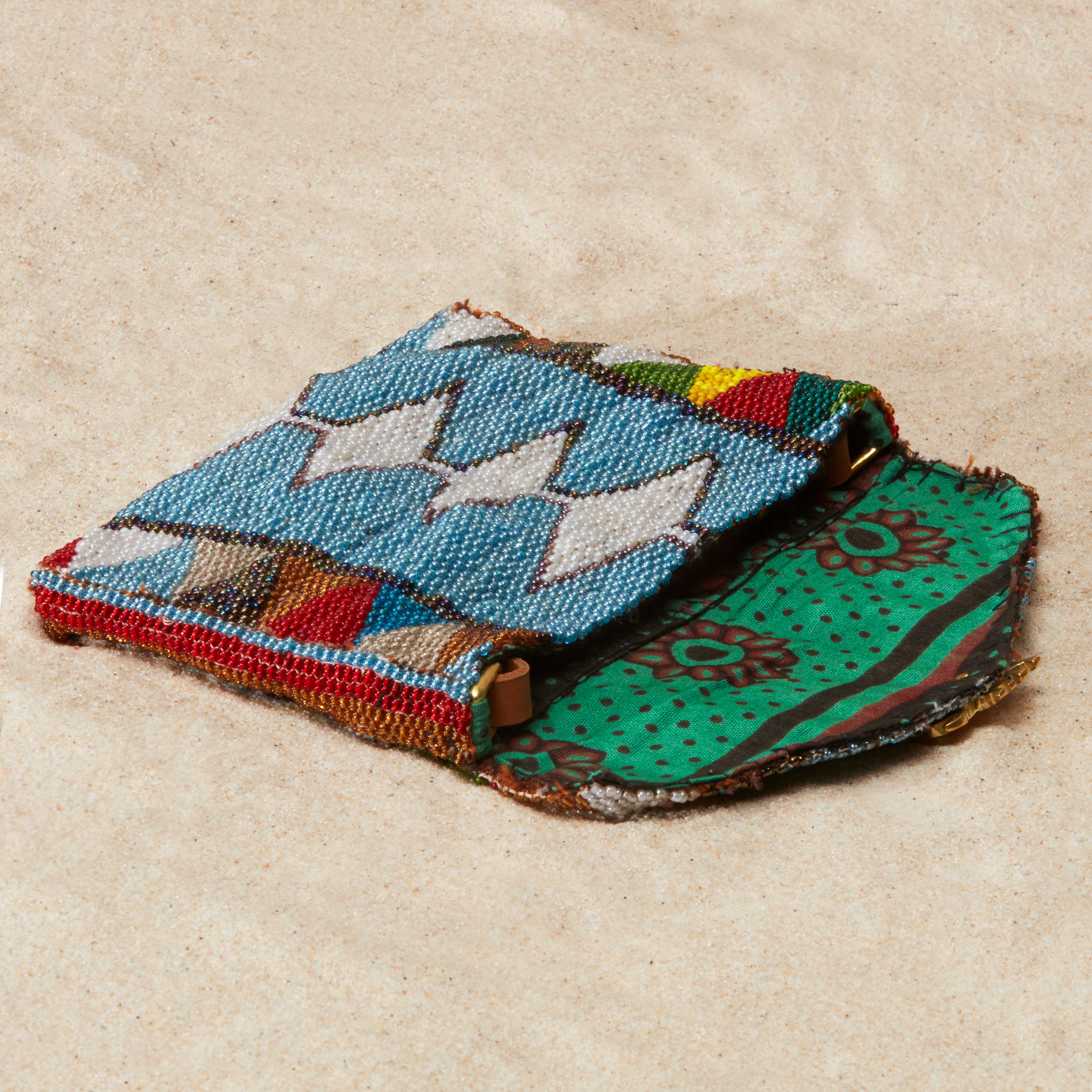 Open colorful beaded pouch with colorful green floral kanga fabric lining on a beige background