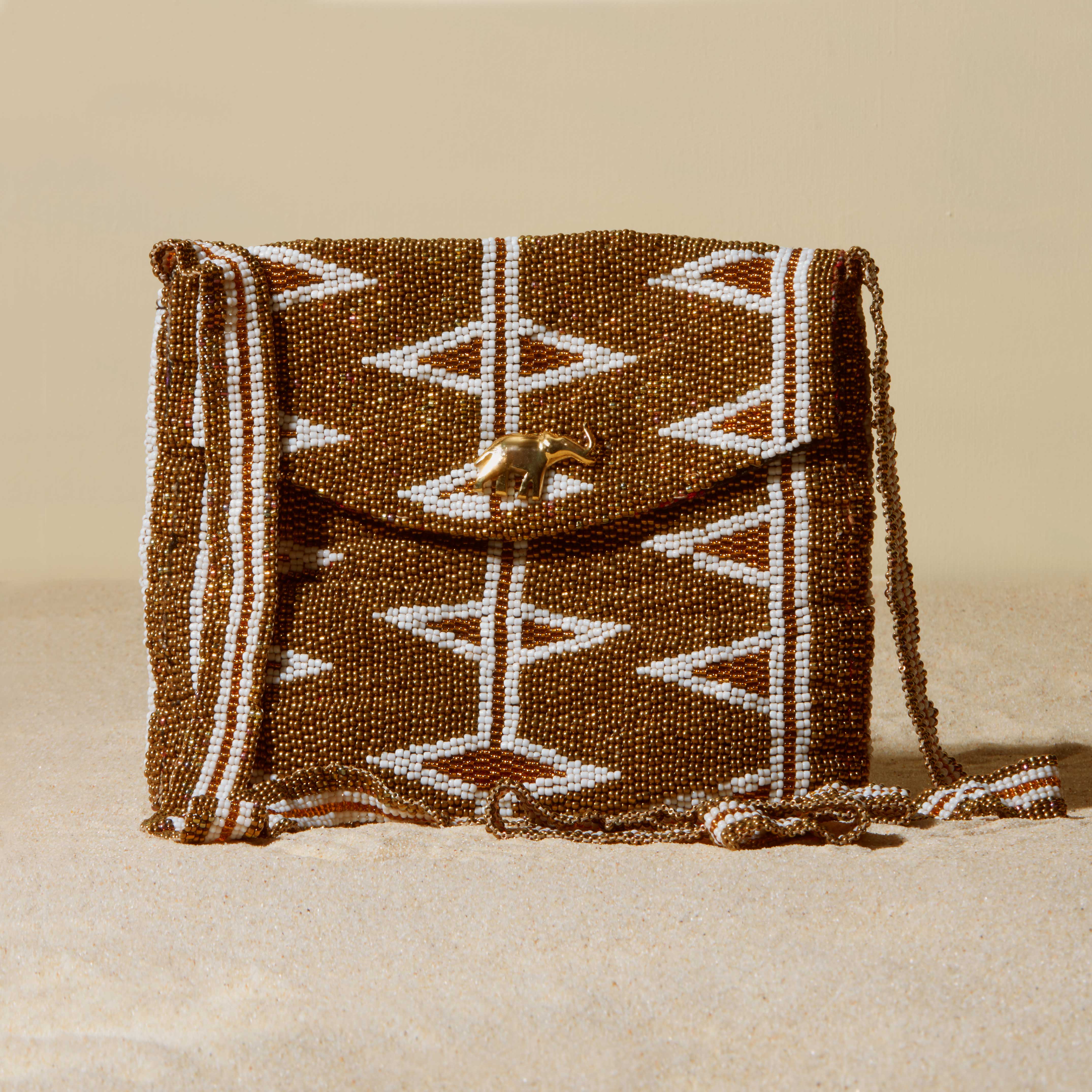 Beaded gold and white handbag with geometric pattern on a sand background