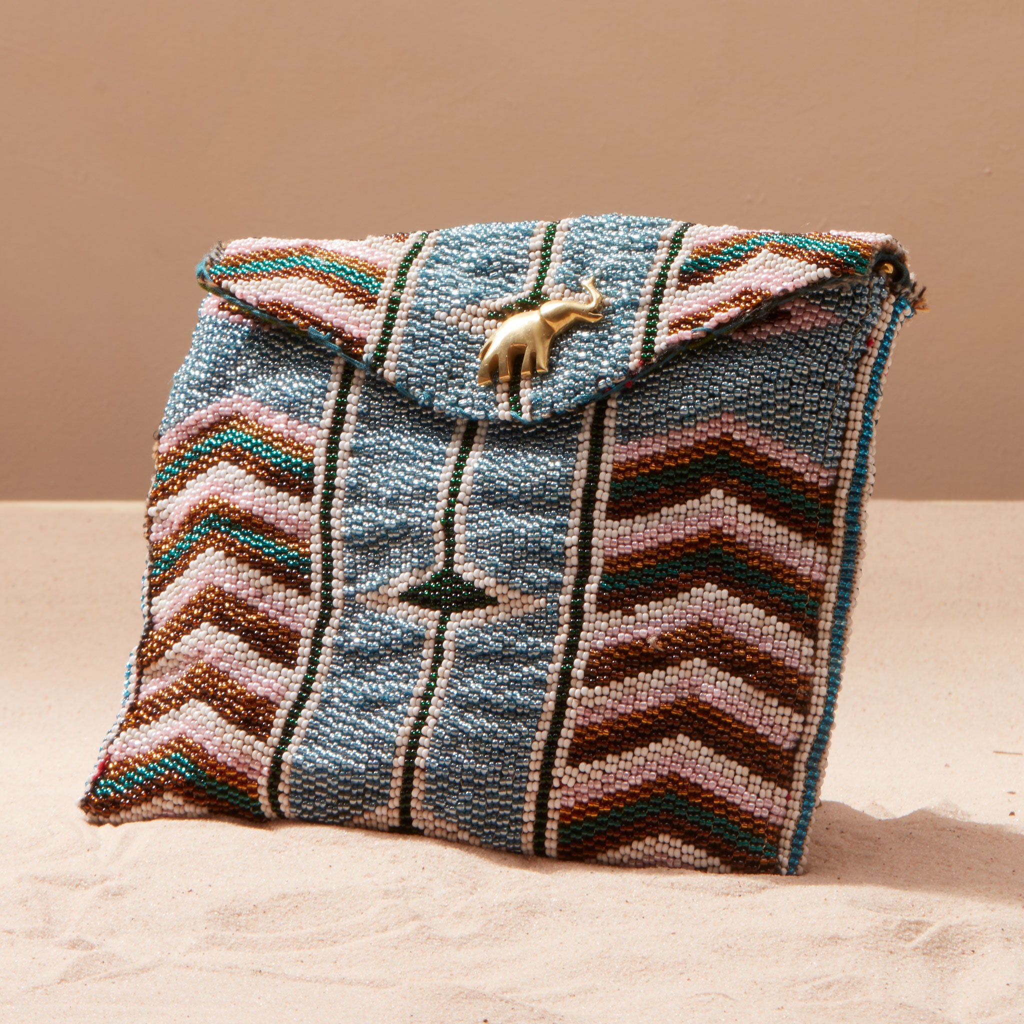 Beaded handbag with geometric pattern and a brass elephant on a sand background