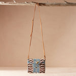 Beaded crossbody bag with a brown leather strap hanging on a branch