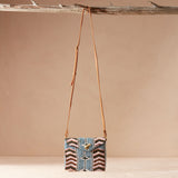 Beaded crossbody bag with a brown leather strap hanging on a branch