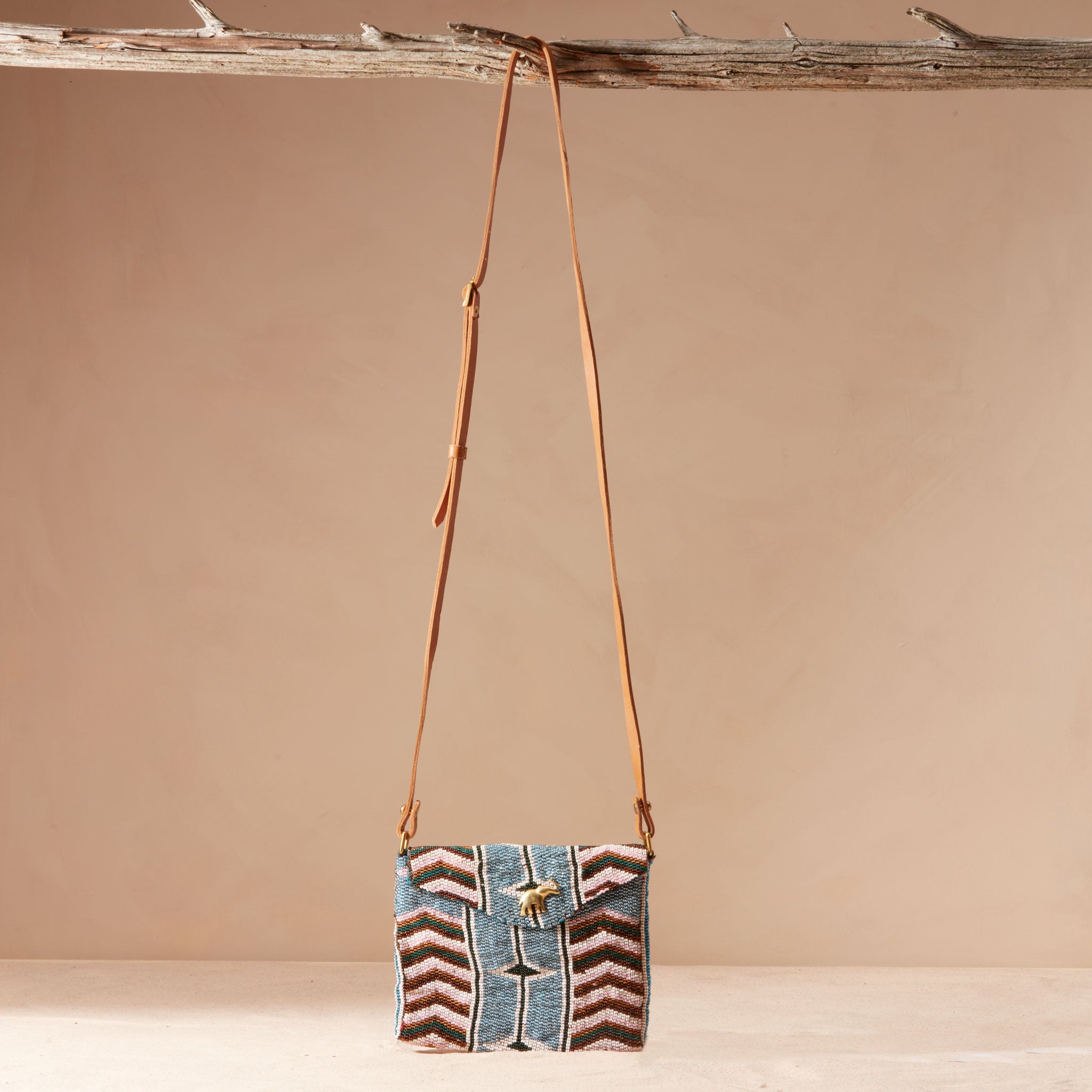 Beaded crossbody bag with a brown leather strap hanging on a branch