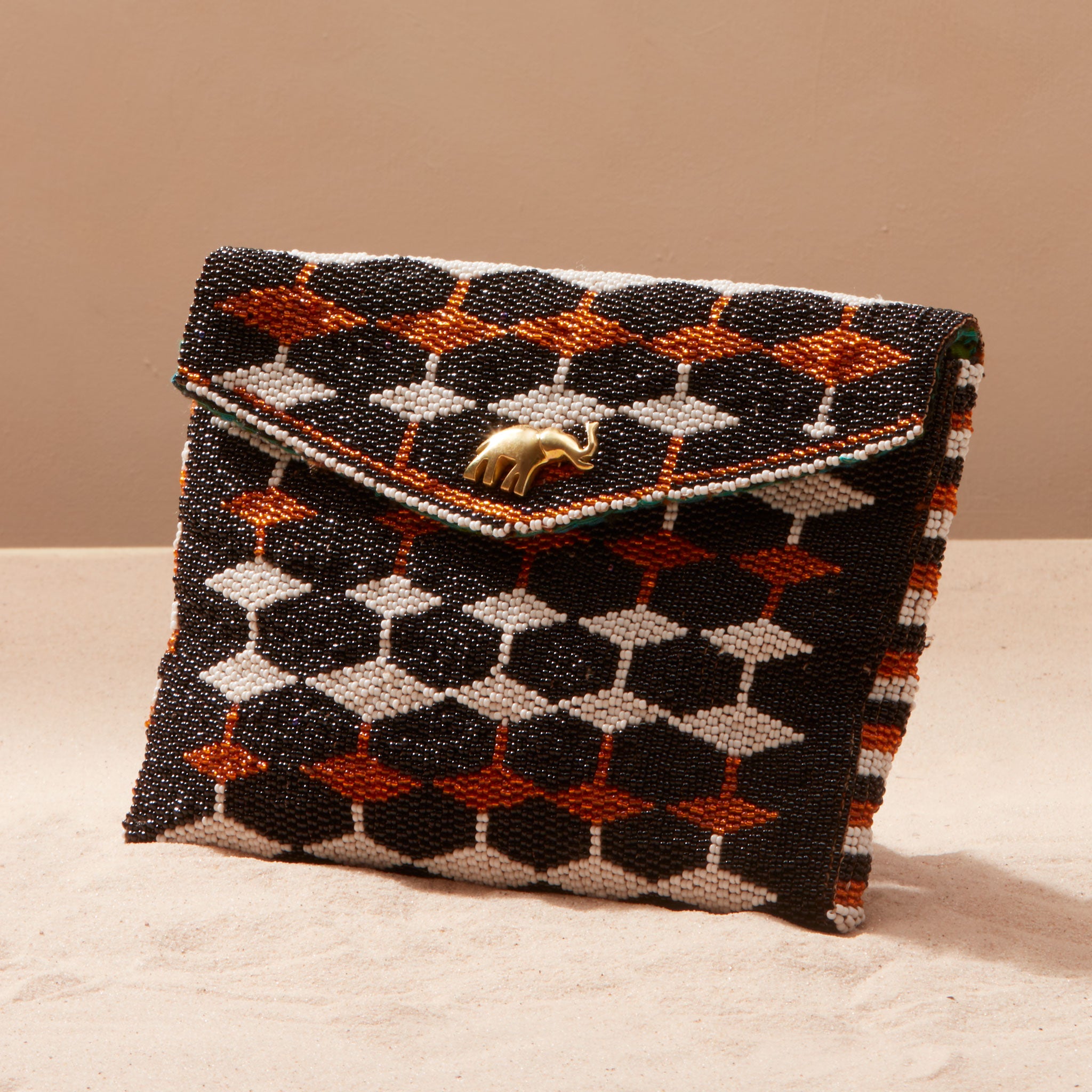 Beaded geometrically patterned handbag with brass elephant on a sand background
