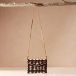 Handbag with geometric pattern and brown leather strap hanging on a branch