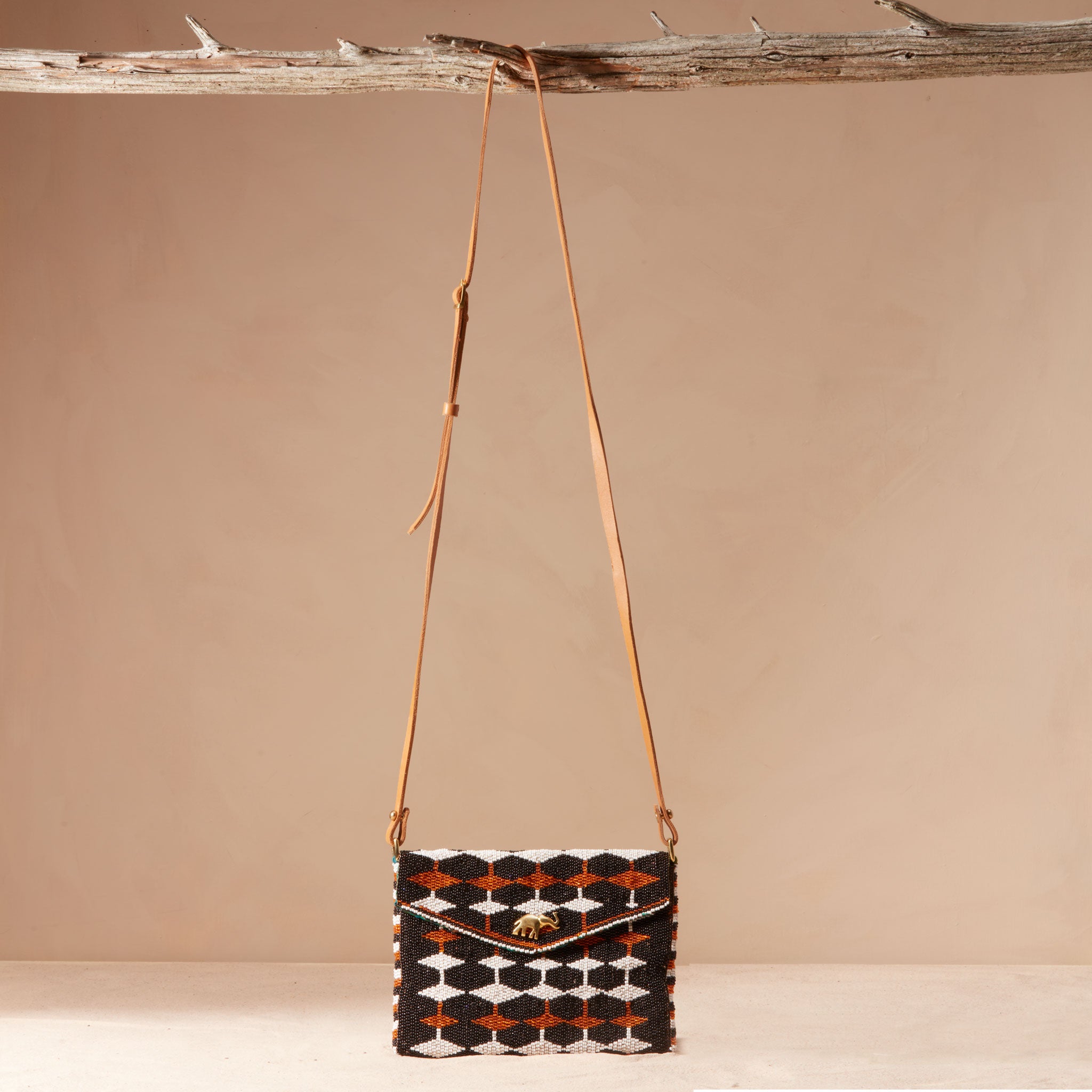 Handbag with geometric pattern and brown leather strap hanging on a branch