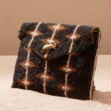 Beaded handbag with geometric pattern and elephant charm on a sand surface